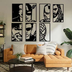 May include: A set of six black metal wall decor pieces featuring the faces of popular superhero characters. The pieces are arranged in a grid pattern on a white wall above a brown sectional sofa.