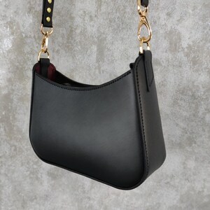 May include: A black leather shoulder bag with a gold chain strap and gold accents. The bag has a curved shape and a smooth finish.