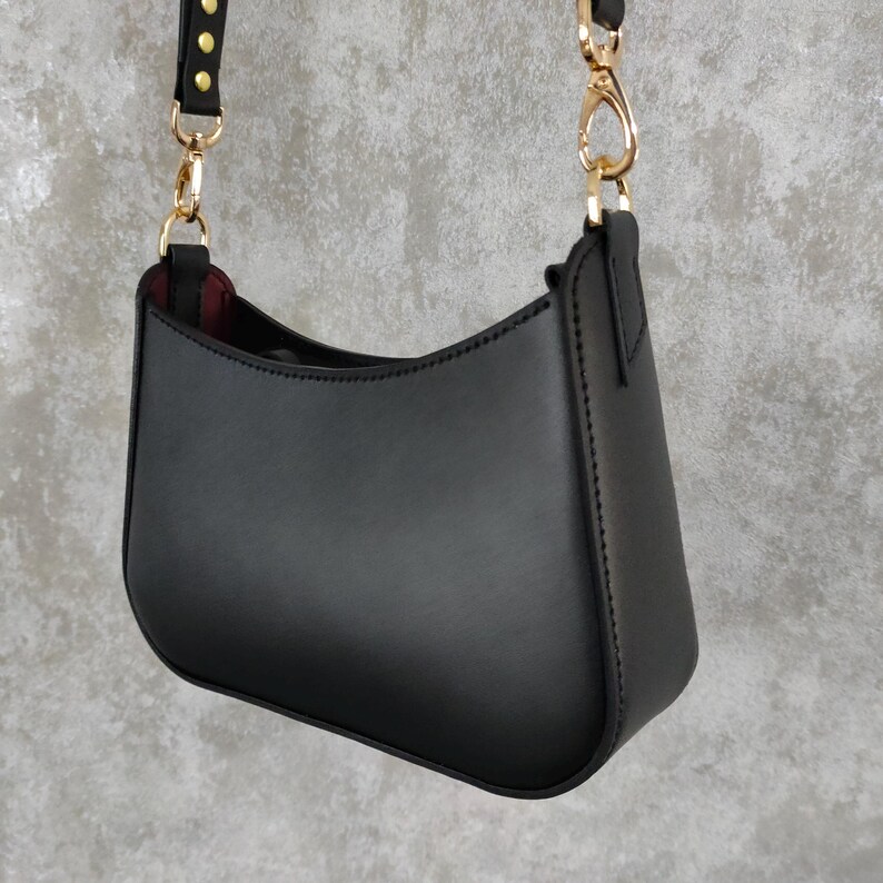 May include: A black leather shoulder bag with a gold chain strap and gold accents. The bag has a curved shape and a smooth finish.