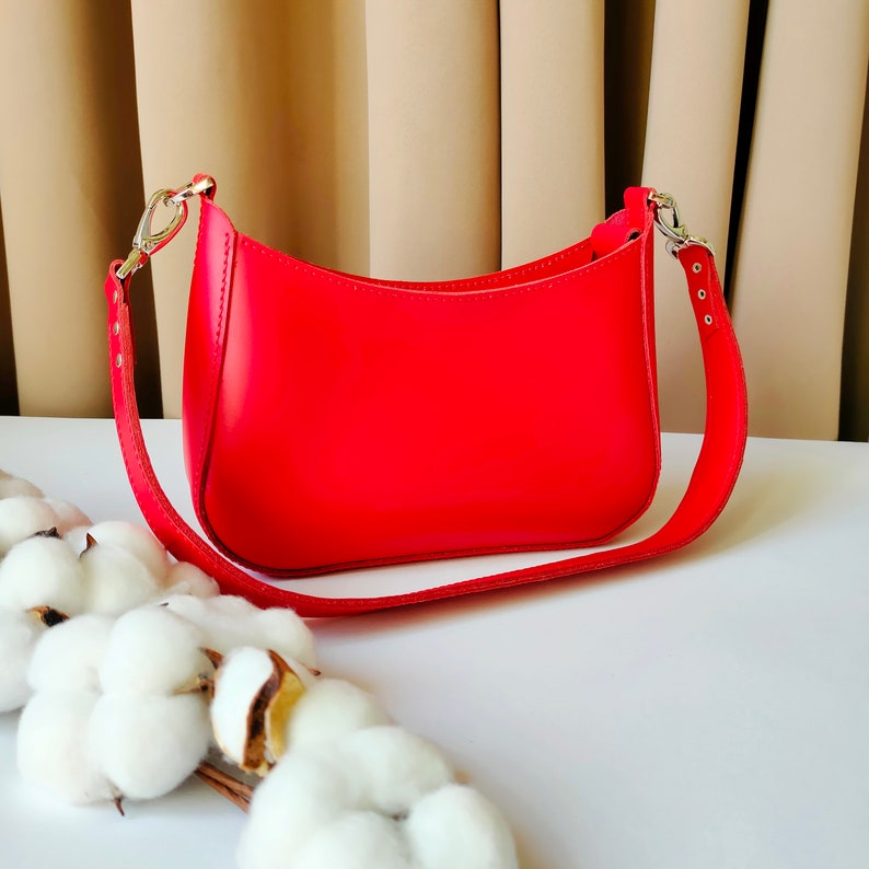 May include: A bright red leather handbag with a shoulder strap. The bag has a curved shape and a simple design.
