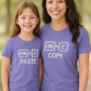 Puede incluir: Dos personas con camisetas moradas a juego. Una camiseta dice "CTRL + V PEGAR" y la otra "CTRL + C COPIAR" en letras blancas. Ambas camisetas tienen cuello redondo y mangas cortas.