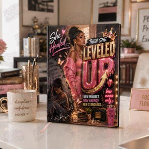 May include: A hardcover journal with the text "She Healed... Then She Leveled Up" in gold and pink. The cover features an illustration of a woman in pink clothing, butterflies, and a crown. A white mug with gold trim and the words "discipline, confidence, success" is also visible.