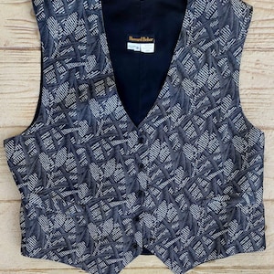Op de afbeelding: Een zwart-wit gepatroneerd vest met een zwarte voering. Het vest heeft een label met de tekst "Howard Behar" en een maatlabel met de tekst "M".
