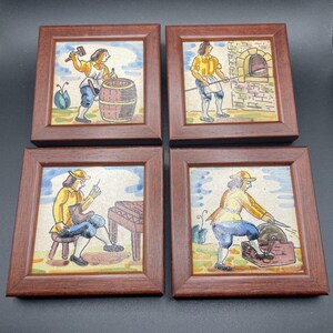 May include: Set of four framed ceramic tiles depicting scenes of people working in different trades. The tiles are painted in a colorful style with a rustic background. The scenes include a person making barrels, a person baking bread, a person working on a wooden table, and a person sharpening a tool.