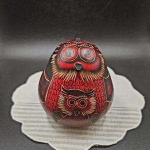 Può includere: Statuetta di gufo intagliata a mano, rossa e nera, con dettagli intricati. Il gufo presenta un design di gufo più grande in alto e un design di gufo più piccolo in basso. Posizionata su un sottobicchiere.