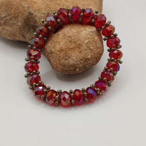 Op de afbeelding: Een rode kristallen armband met gouden accenten. De armband is gemaakt van kleine, gefacetteerde kralen die aan elkaar geregen zijn op een draad.