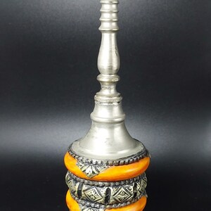 May include: A silver and orange decorative bottle with a tall, slender neck and a round base. The bottle is decorated with intricate metalwork and orange bands.