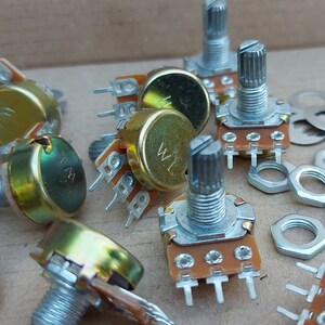 May include: A group of gold-coloured potentiometers with silver knobs and a set of silver nuts and washers. The potentiometers have multiple pins on the bottom and are used for adjusting electrical resistance.