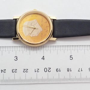 May include: A gold-toned wristwatch with a black leather band. The watch face has a gold background with a white design. The band is approximately 9 inches long.