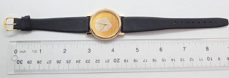 May include: A gold-toned wristwatch with a black leather band. The watch face has a gold background with a white design. The band is approximately 9 inches long.