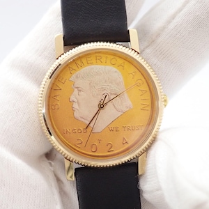 May include: Gold-toned wristwatch with a black leather band. The watch face features a gold coin design with the text "SAVE AMERICA AGAIN" and the year "2024". The watch has gold-colored hands and a gold-colored bezel.