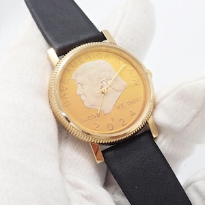 May include: Gold-toned wristwatch with a black leather band. The watch face features a gold coin design with a profile portrait, the text "SAVE AMERICA AGAIN", "IN GOD WE TRUST", and the year "2024".
