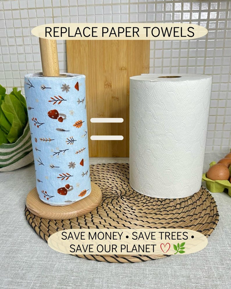Op de afbeelding: Een lichtblauwe herbruikbare keukenrol met een paddenstoelen- en bladerpatroon op een houten houder naast een standaard witte keukenrol. Tekst: REPLACE PAPER TOWELS, =, SAVE MONEY &bull; SAVE TREES &bull; SAVE OUR PLANET met een hartje en een blaadje.