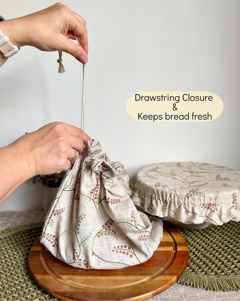 May include: A beige fabric bread bag with a drawstring closure and a botanical pattern of small red berries and green stems. The text on the image reads Drawstring Closure & Keeps bread fresh. A matching fabric bowl cover is also visible.