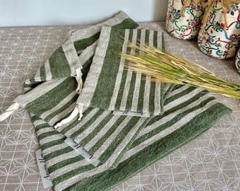 Puede incluir: Un conjunto de tres bolsas de tela con cierre de cordón que presentan un patrón de rayas verticales en verde oliva y blanco roto. Cada bolsa tiene un cordón blanco y una pequeña etiqueta blanca con el texto Anisenia Home en el lateral.