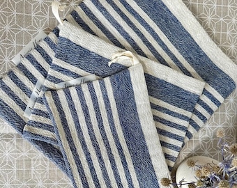 Puede incluir: Varios paños de cocina a rayas azules y blancas están cuidadosamente colocados sobre una superficie estampada. Cada paño tiene un lazo para colgar y una etiqueta que dice "Anisnia Home". Los paños están hechos de tela texturizada.