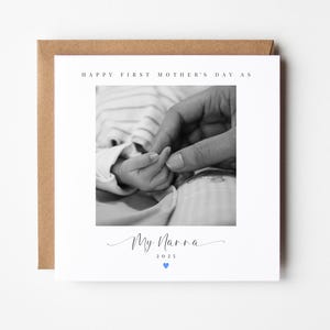 May include: A black and white photo of a baby's hand holding the finger of an adult. The card reads "Happy First Mother's Day as My Nanna 2023" with a blue heart.