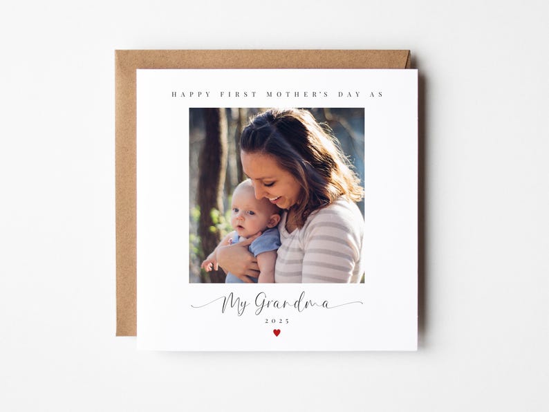 May include: A white card with a photo of a woman holding a baby. The text on the card reads "Happy First Mother's Day as My Grandma 2023" with a small red heart.