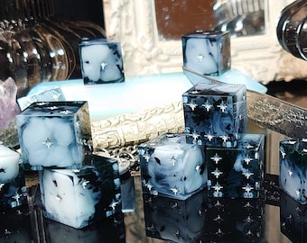 May include: A set of 10 black and white dice with a cloudy, galaxy-like design. The dice are scattered on a black surface with a reflection of the dice visible.
