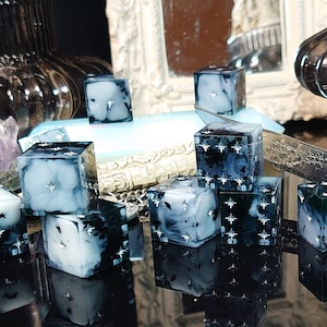 Puede incluir: Un conjunto de 10 dados negros y blancos con un diseño nublado, similar a una galaxia. Los dados están esparcidos sobre una superficie negra con un reflejo de los dados visible.