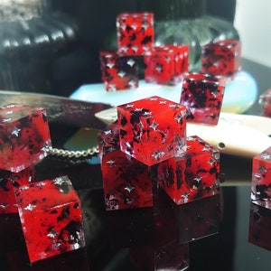 K&ouml;nnte beinhalten: Eine Gruppe roter W&uuml;rfel mit schwarzen und silbernen Flecken. Die W&uuml;rfel sind auf einer schwarzen Oberfl&auml;che verstreut.