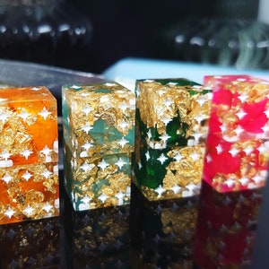 Könnte beinhalten: Vier kleine quadratische Boxen mit Goldblattakzenten und weißen Sternen. Die Boxen sind orange, grün, dunkelgrün und rot.