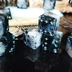 Pode incluir: Um conjunto de seis dados preto e branco com glitter prateado embutido na resina. Os dados t&ecirc;m um aspecto nublado e marmorizado.