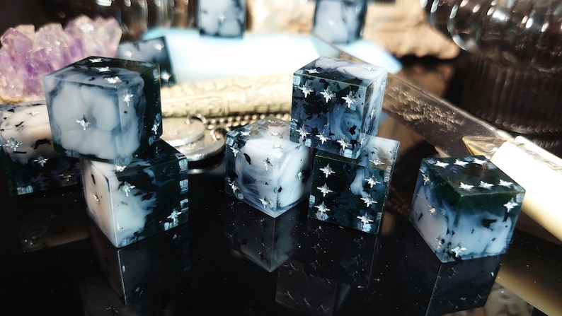 Pode incluir: Um conjunto de seis dados preto e branco com glitter prateado embutido na resina. Os dados t&ecirc;m um aspecto nublado e marmorizado.