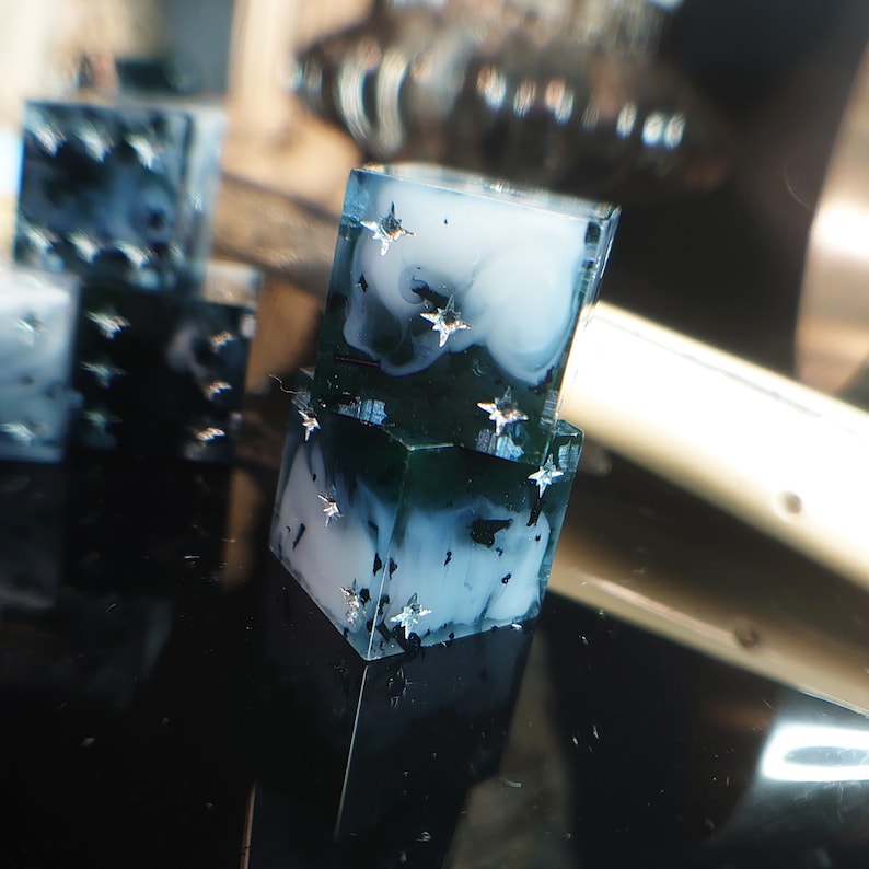 Pode incluir: Dois dados de resina transparente empilhados com um efeito marmorizado azul e branco e estrelas prateadas brilhantes.