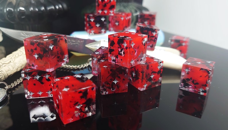 K&ouml;nnte beinhalten: Ein Satz roter W&uuml;rfel mit schwarzen und silbernen Flecken. Die W&uuml;rfel sind durchsichtig und haben eine gesprenkelte Optik.