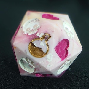 Op de afbeelding: Een twintigzijdige dobbelsteen met een gemarmerde witte en roze basis. Het oppervlak bevat ingelegde ontwerpen, waaronder witte schedels, felroze harten en een goudkleurige toverdrankfles met een witte vloeistof in het midden van de hars.