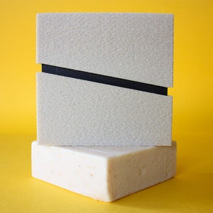 Puede incluir: Una caja rectangular blanca con una línea diagonal negra en la parte superior. La caja está colocada sobre un bloque rectangular blanco.