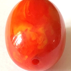 May include: An oval-shaped bead with a smooth, polished surface. The bead features a vibrant, marbled color pattern blending shades of bright orange and deep red throughout its structure. A single circular hole is visible near the bottom edge.