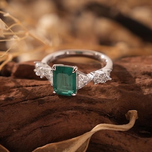 Può includere: Un anello d'argento con una grande pietra preziosa verde smeraldo e piccoli accenti di diamanti.