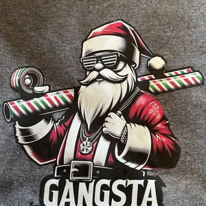 Könnte beinhalten: Graues T-Shirt mit einer Grafik von Santa Claus mit Sonnenbrille und rotem Anzug, der Zuckerstangenrollen trägt. Der Text "Gangsta Wrapper" ist darunter gedruckt.