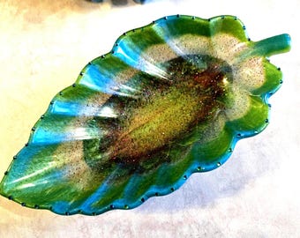 May include: A leaf-shaped decorative tray featuring a swirling blend of vibrant green, turquoise, and deep brown resin. The surface is embedded with fine glitter particles throughout, and the scalloped edges are accented with small, dark beads.
