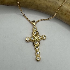 May include: A gold chain necklace with a small, ornate cross pendant. The cross is decorated with clear cubic zirconia stones.