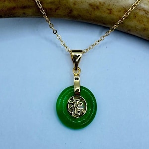 May include: A gold chain necklace with a green jade pendant featuring a Chinese character. The pendant is round and has a gold rim.