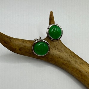 Op de afbeelding: Een paar zilveren oorbellen met groene cabochons. De oorbellen worden getoond op een stuk geweihorn.