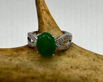 May include: A silver ring with a green oval gemstone and clear cubic zirconia accents.