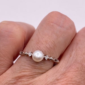 May include: A silver ring with a single white pearl and small clear stones set in a delicate vine design.