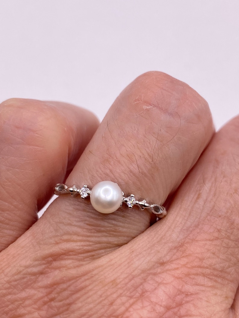 May include: A silver ring with a single white pearl and small clear stones set in a delicate vine design.