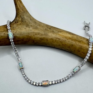 May include: A silver bracelet with a row of clear cubic zirconia stones and four rectangular opal stones.