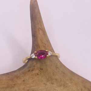 以下が含まれることがあります： ピンクの楕円形の宝石と2つの小さな透明な宝石が付いた金の指輪