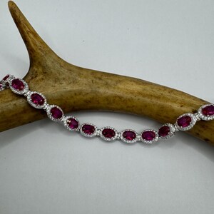 May include: A silver bracelet with a row of oval-shaped ruby stones set in a halo of diamonds.