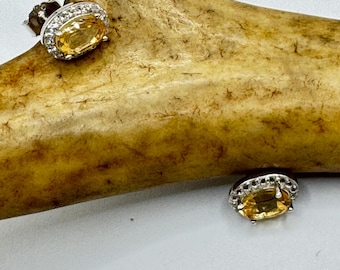 May include: A pair of silver earrings with oval-shaped yellow gemstones surrounded by a halo of smaller white gemstones.