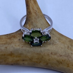 May include: A silver ring with three oval-shaped green gemstones and two smaller clear gemstones.