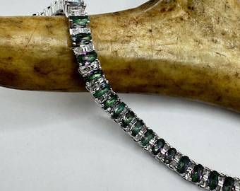 May include: A silver bracelet featuring a series of oval-cut, iridescent green gemstones. The bracelet is set against a light background and a section of a brown antler.