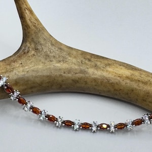 May include: A silver bracelet with alternating brown and clear oval-shaped stones. The bracelet is displayed on a light brown antler.