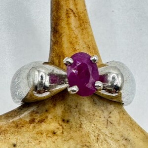 May include: A silver ring with a large, oval-shaped, pink ruby gemstone.
